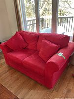 Full view of red faux suede loveseat showing pillow back cushions and two throw pillows.
