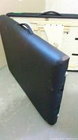 Black massage table folded upright showing padded surface and carrying handle.