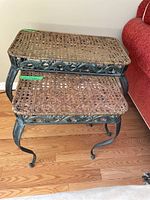 Photo showing set of two metal frame nesting tables with wicker tops, placed on wooden floor near red couch.