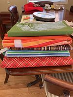 Stack of five folded plastic table cloths in various colors and patterns including green, orange, red, blue, and carrot design.