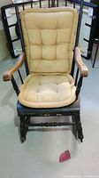 Front view of black wooden rocking chair with beige cushions showing seat and backrest with tufting detail.