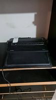 Canon ES 10 typewriter with a cover on keyboard and handle, shown from front and side angles on a wooden surface.