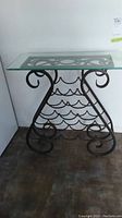 Full view of the wine holder table showing its clear glass top and black metal scrollwork base with wine bottle holders.
