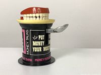 Side view of the novelty bank showing the red mouth closed and spoon attached on the side.