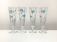 Four mid century atomic beer glasses in a row, showing front view and printed geometric designs in blue, gold, and black.