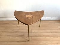 Front angled view showing triangular teak wood table top with central tile inlay and three brass legs.