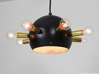 Black painted metal hemispherical mid century pendant lamp with six brass bulb holders and exposed clear bulbs, photographed hanging from ceiling.