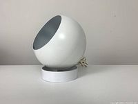 Front-side view of white spherical spot lamp with cord coiled beside base on white surface.