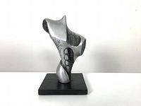 Front view of the aluminum sculpture showing abstract form and wood base