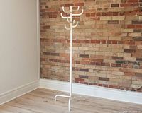 Full view of the white enamelled steel coat tree standing on a light wood floor against a brick wall.