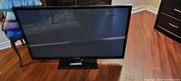 Front view of Samsung 52 inch Plasma TV turned off, showing the screen, black bezel, and the base stand with remote control.