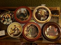 Six Norman Rockwell collectible plates displayed face-up in wooden frames showing various classic scenes such as "Romantic Reverie," "Quiet Reflections," "Grandma's Love," "Grandpa's Gift," "Mother's Day 1988," and "Scarlett and Her Suitors."