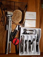 Photo showing silver camera tripod, black wall shelf, various kitchen tools including can opener, jar gripper, potato masher, woven trivets, cutlery organized in tray, and two photo albums.