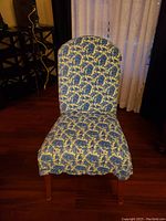 Front view of a padded upholstered chair with blue and gold patterned fabric and wooden legs, placed against a curtain background