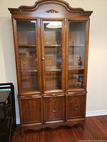 Front view of the wooden china cabinet with three glass doors on top and three wooden doors at the bottom, showing overall design and condition.
