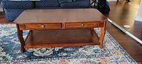 Front view of rectangular wooden coffee table on patterned rug, showing two small drawers with metal knobs and lower shelf.