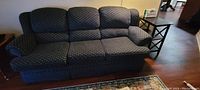 Full view of blue fabric couch with three seat cushions and rounded armrests on a wood floor