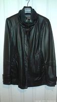 Front view of mid-length black leather coat showing smooth black leather, button front closure, snap flap pockets, and sweater lining visible at neck and wrists.