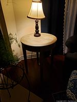 Side view of the round wooden side table with a lamp on top showing shape and leg style.