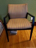 Front view of the chair showing striped seat and back upholstery with black wooden frame and armrests.