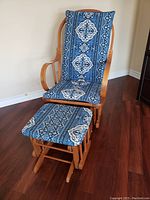 Front view of the wooden glider rocking chair with blue patterned cushions and matching ottoman on hardwood floor.