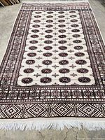 Full view of cream rug with red and brown medallion pattern and fringe edges