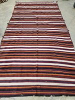 Full view of the flat woven Kelim rug showing horizontal stripes in multiple colors on a concrete floor.