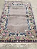 Full view of the rug showing the central plain field and detailed floral border with fringed edges.