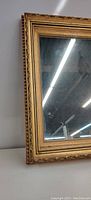 Close-up of the ornate gold frame corner showing carved leaf and bead detail around the mirror glass edge.