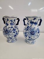 Front view of the pair of blue and white ceramic vases with floral pattern and dual handles.