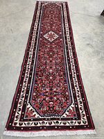 Full length view of runner on concrete floor showing red field, borders and white fringe at ends