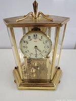 Front view showing white dial with black Arabic numerals and floral design inside a hexagonal brass frame with glass panels.