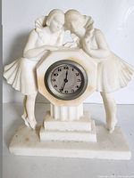 Front view of the vintage stone clock with two figurines and the clock face showing black numerals and hands.