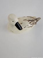 Angle showing front and side of wooden duck figurine with black painted beak and white body with distressed black feather markings.