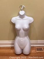 Front view of slim female torso mannequin in bright white plastic on floor, showing detailed smooth contours and slim body shape.