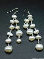Front view of the freshwater pearl drop earrings, showing the irregular shapes and sizes of the pearls, strung on silver threads and hanging from silver tone hooks.