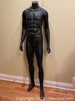 Full view of the assembled mannequin, showing slim black male figure with defined muscles and no stand, positioned against wall on hardwood floor.