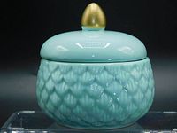 Front view of turquoise porcelain jar with mermaid scale pattern and smooth lid with gold knob on top.