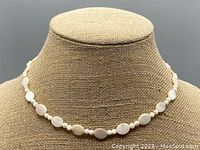 Full view of the mother of pearl bead necklace displayed on a beige textured bust stand.