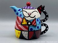 Front view of colorful Romero Britto cat teapot with cup stacked, showing vibrant cubism and pop art style patterns.