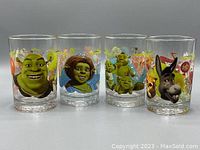 Front view of all four collectible McDonalds glasses showing major characters including Shrek, Princess Fiona, Donkey, and Puss in Boots with colorful movie-themed designs.