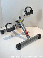 Side angle view showing folding pedal exerciser with foot straps and tension control knob on silver metal frame.
