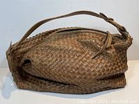 Front view of the brown woven leather shoulder bag showing the zipper and single strap handle with knots at ends.