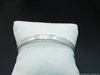 Front view of smooth luminous cream white mother of pearl bangle resting on white pillow against black background