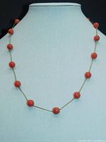 Front view of coral bead necklace displayed on mannequin with coral beads evenly spaced on gold chain