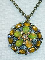 Close-up image showing the detailed round pendant with yellow/green opal-like stones, bronze-colored stones, filigree work, enamel, and aurora borealis accent stones on a bronze-colored chain.