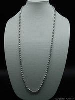 Full view of a long strand vintage necklace composed of uniform dove gray pearls, displayed on a white bust stand to show length and drape.
