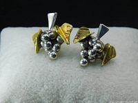 Pair of vintage grape cluster earrings showing silver-colored hollow grapes with gold-colored leaves with etched veins, placed on a white cushion.