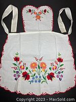 Front full view of white cotton apron with colorful traditional Kalocsa floral embroidery, showing waist ties and scalloped edges with red trim.