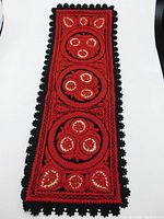 Full view of the rectangular red and black felt table runner showing the symmetrical folk art floral patterns and black leaf-trimmed edges.